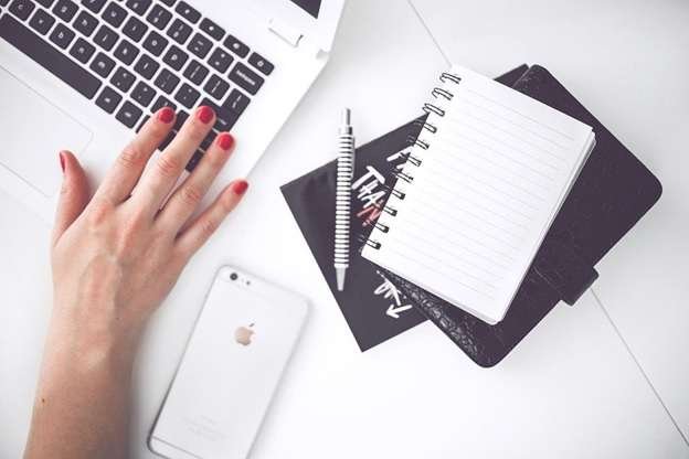 A person using a laptop at work with a notepad and phone on the desk