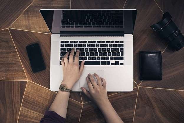 A woman using a laptop with an iPhone, wallet, and lens on a desk