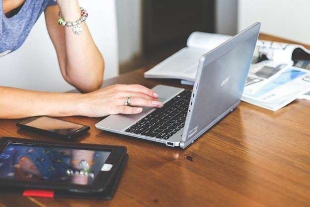 A woman using a laptop with books, a tablet, and a phone on the table
