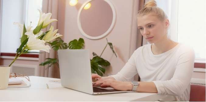 A young woman using a laptop with plants in the background