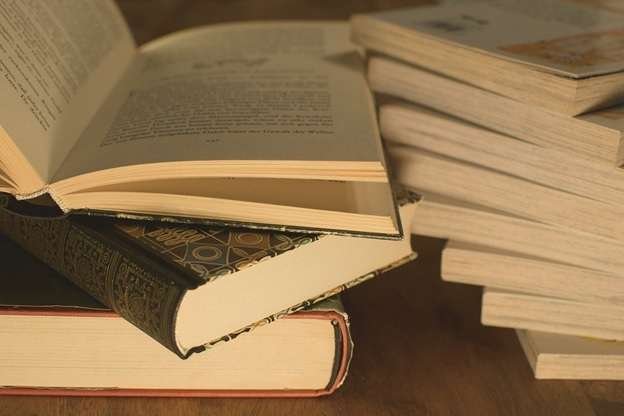 Piles of books placed on top of a wooden surface